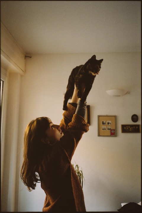 A woman holds a cat up in the air, looking up at it.