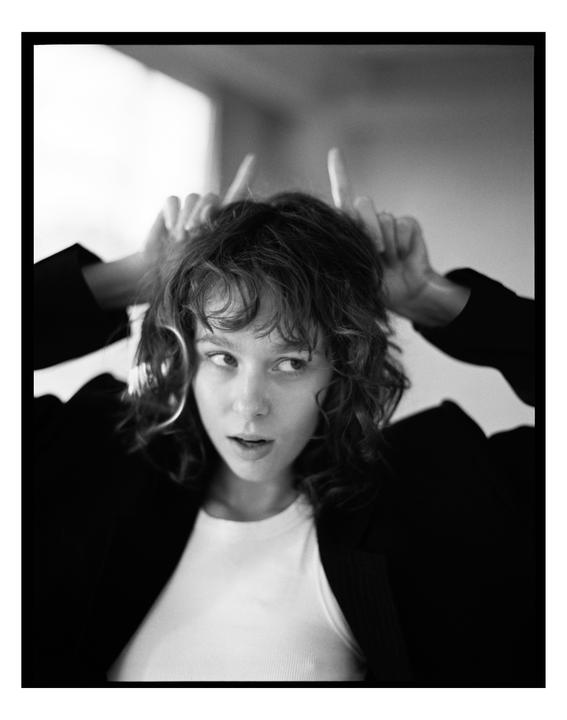 A woman with curly hair holds her hands above her head to mimic horns.