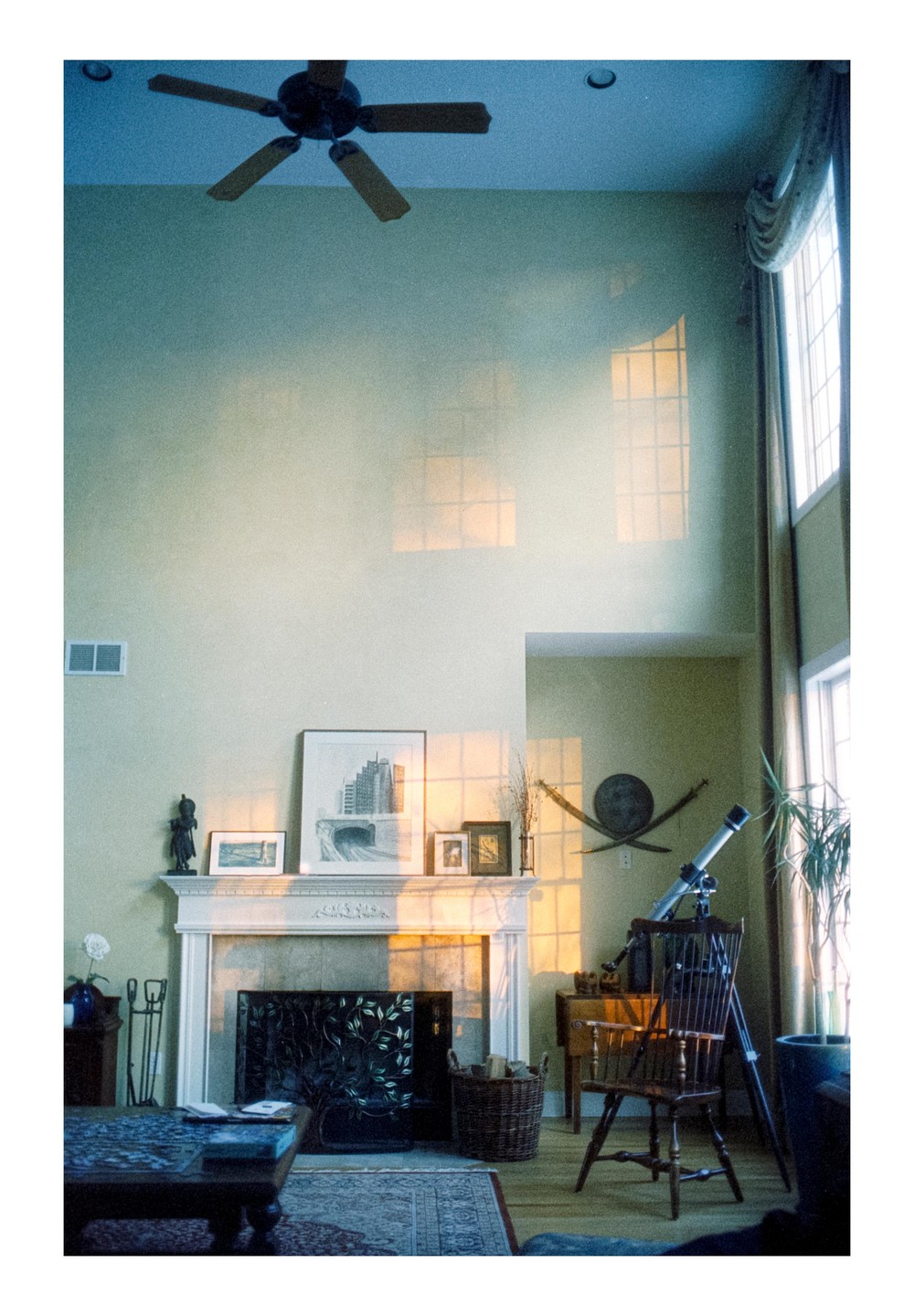 Sunlight streams through a window, casting a grid pattern on the wall above a fireplace and a telescope in a living room.