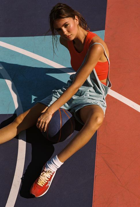 A woman sits on a colorful basketball court, holding a basketball.
