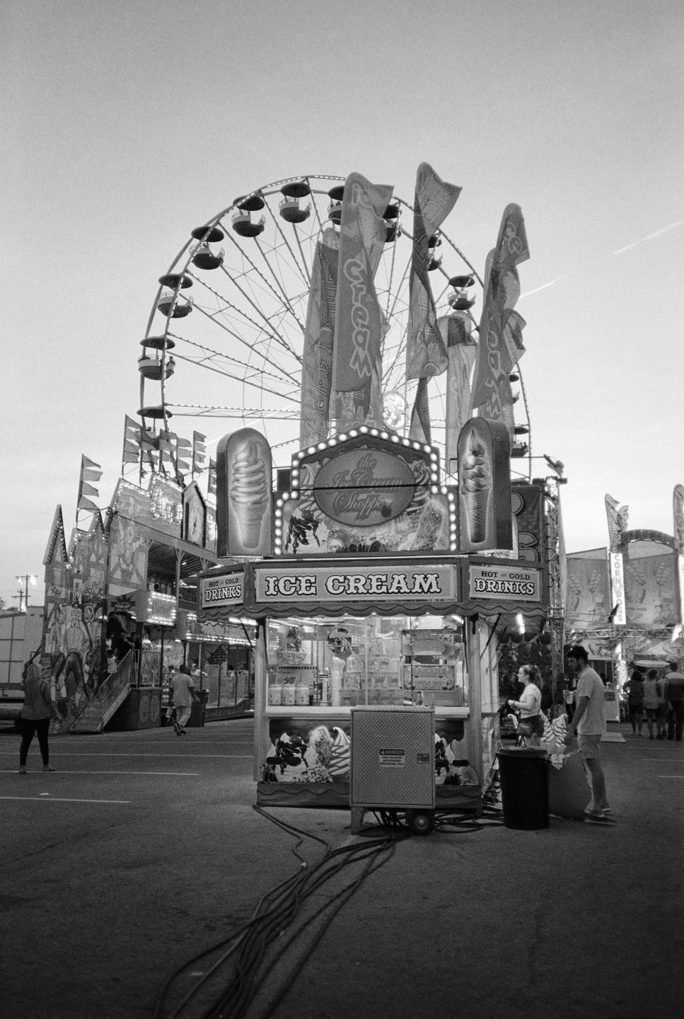 A ferris wheel rises above an ice cream stand at a fairground.