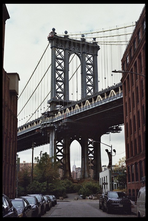 The Manhattan Bridge is framed by buildings on either side, with the Empire State Building visible through its archway.