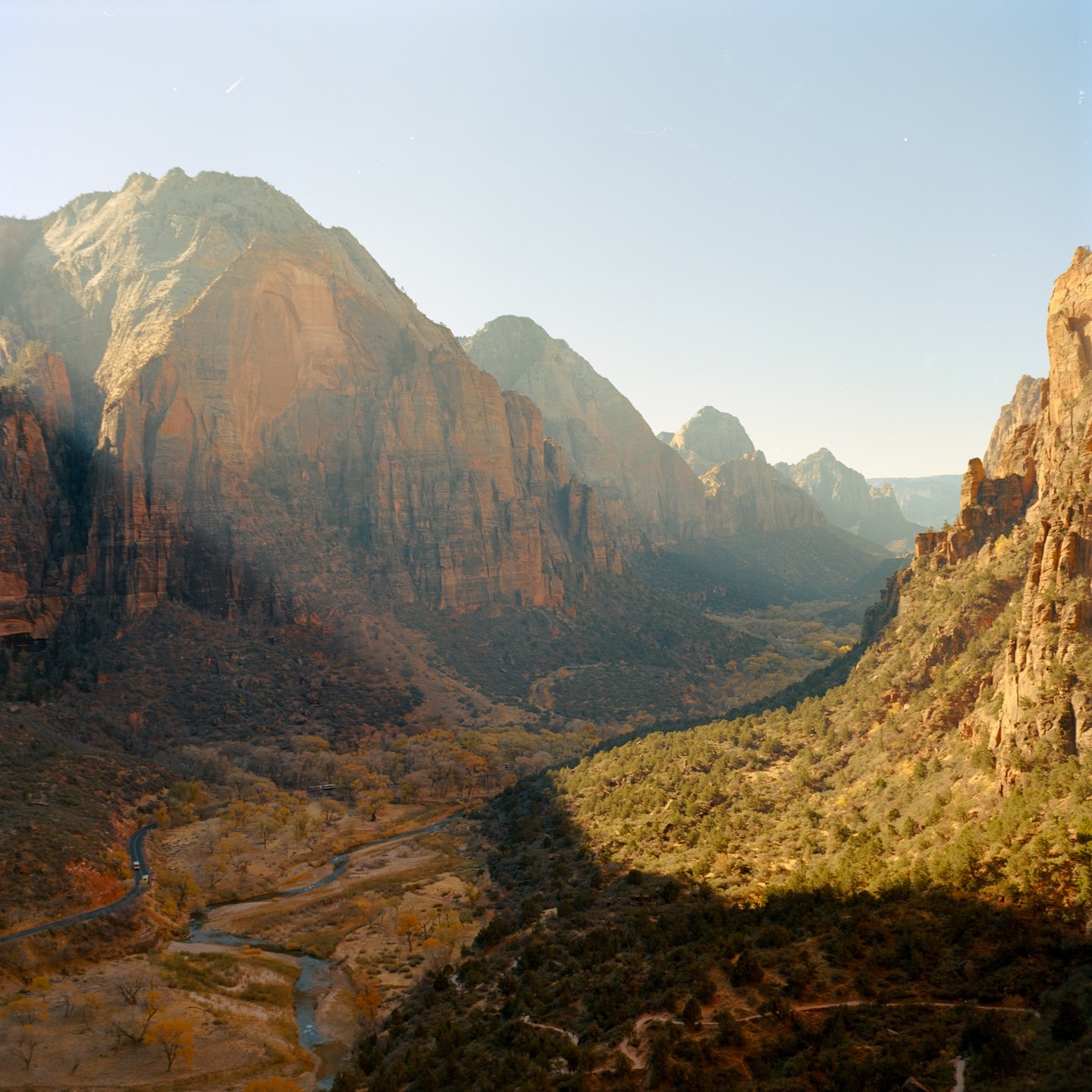 A winding river and road cut through a valley surrounded by towering mountains.