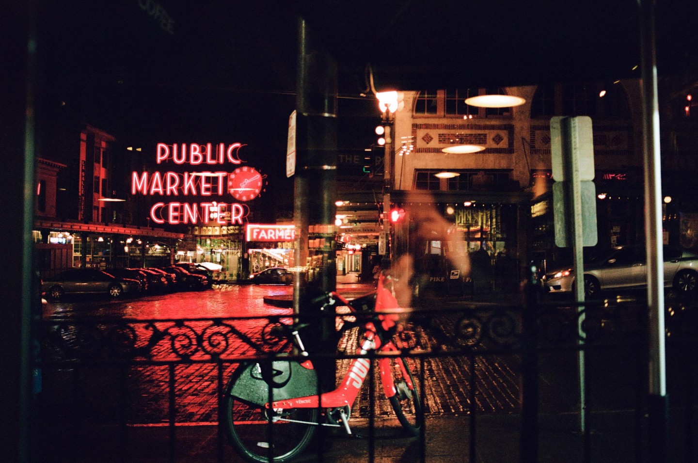 A red bicycle is parked in front of a building with a neon sign that reads "Public Market Center" at night.