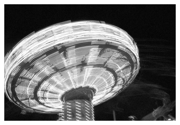 A long exposure shot captures the spinning lights of a carnival ride at night.