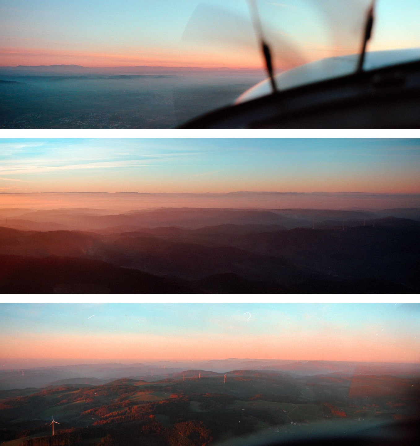 A panoramic view of the Black Forest from above at sunset, with rolling hills, scattered wind turbines, and a hazy sky.