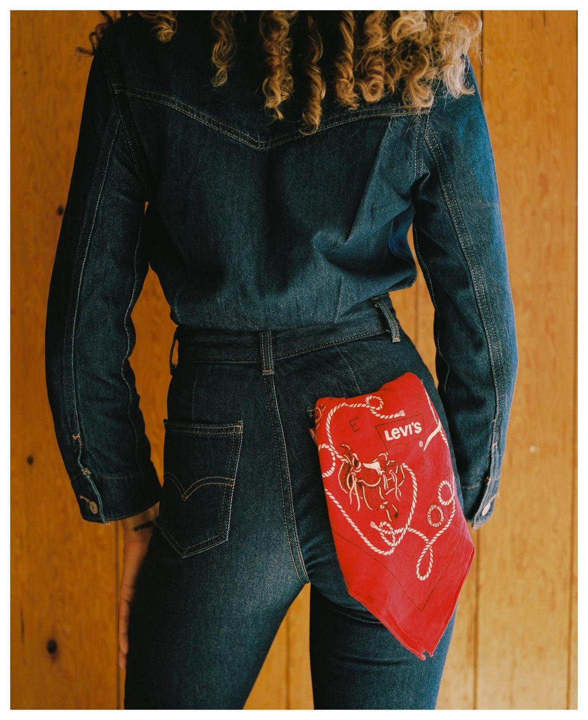 A woman wearing a denim shirt and jeans has a red bandana with a Levi's logo in her back pocket.