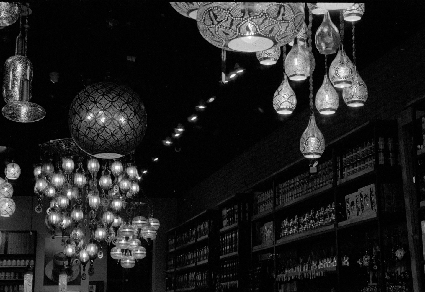 Many ornate lamps hang from the ceiling, illuminating shelves of products in a store.