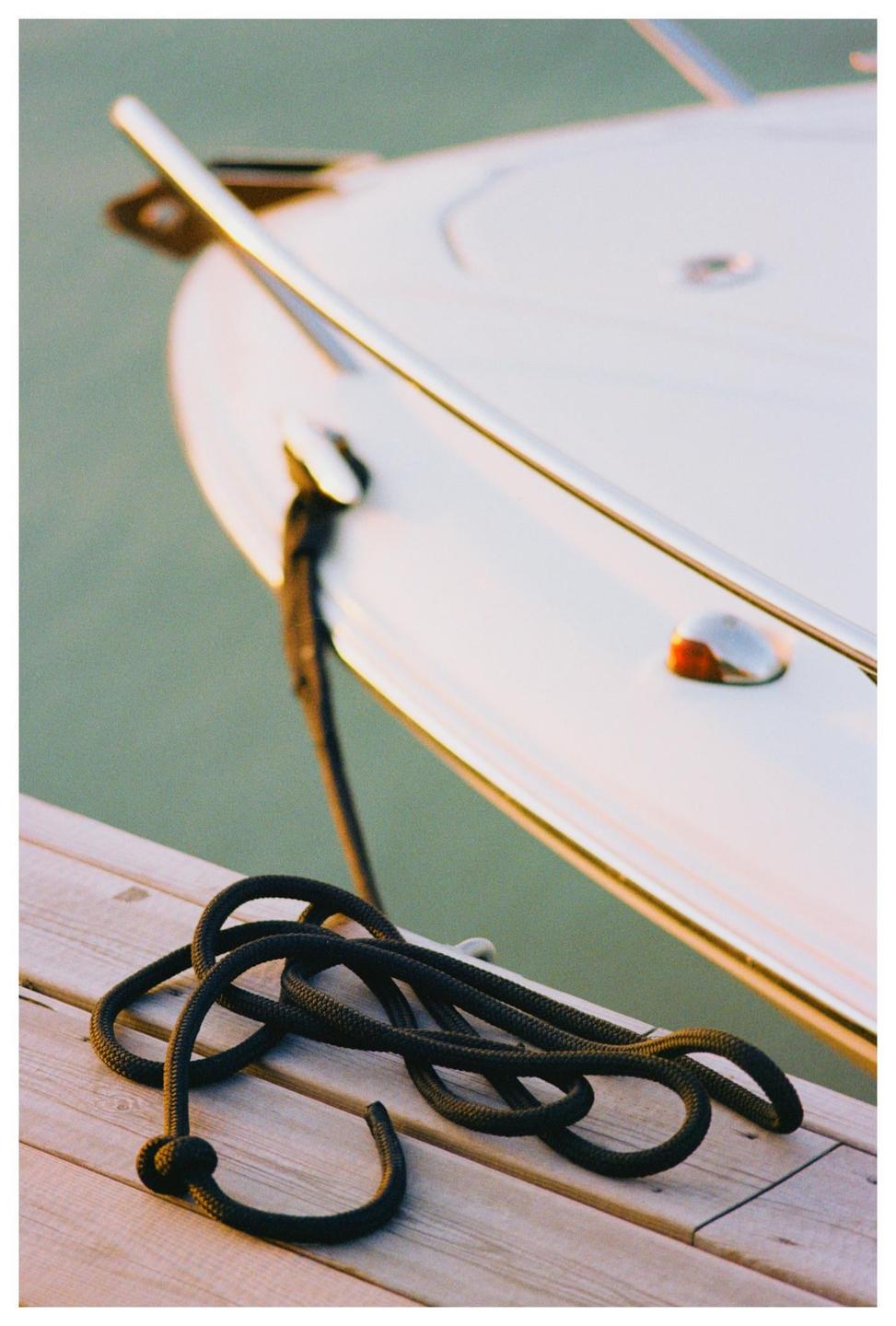 A black rope is coiled on a wooden dock next to a white boat.