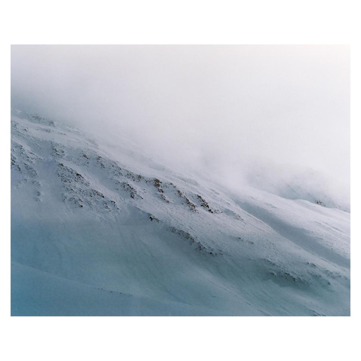 A snow-covered mountain slope is partially obscured by fog.