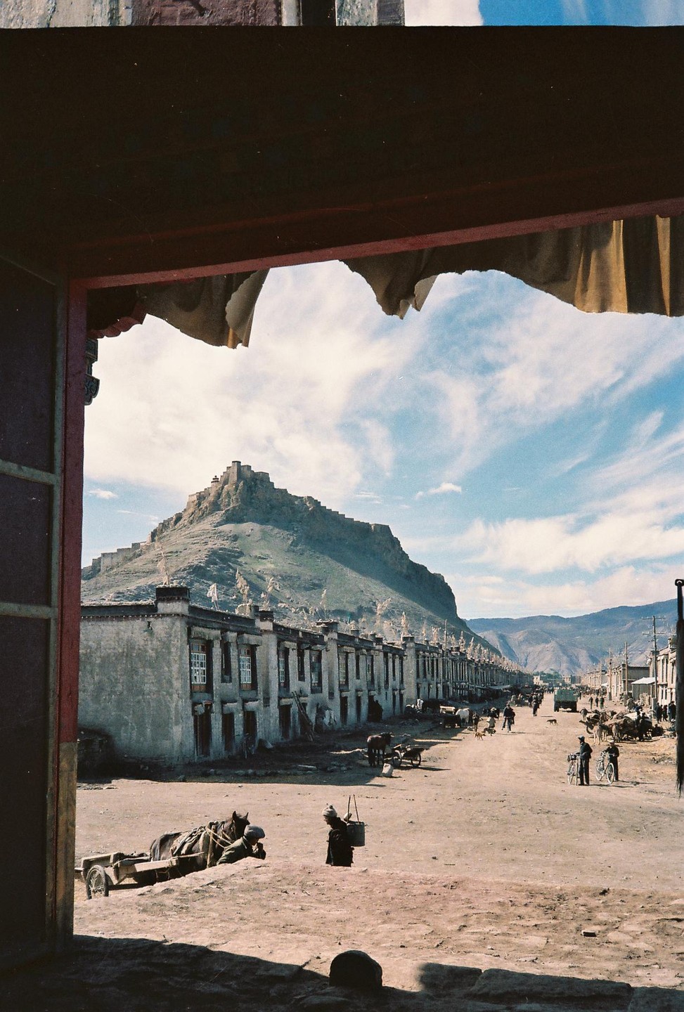 A street in Gyantse is framed by a doorway, with a mountain and buildings in the background.