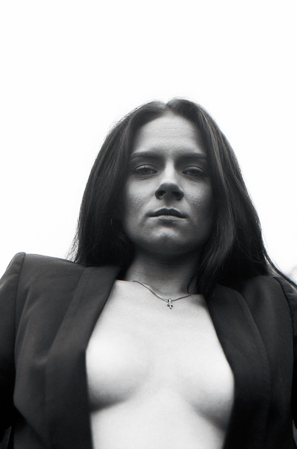 A woman with long hair and a necklace is wearing a jacket and looking directly at the viewer.