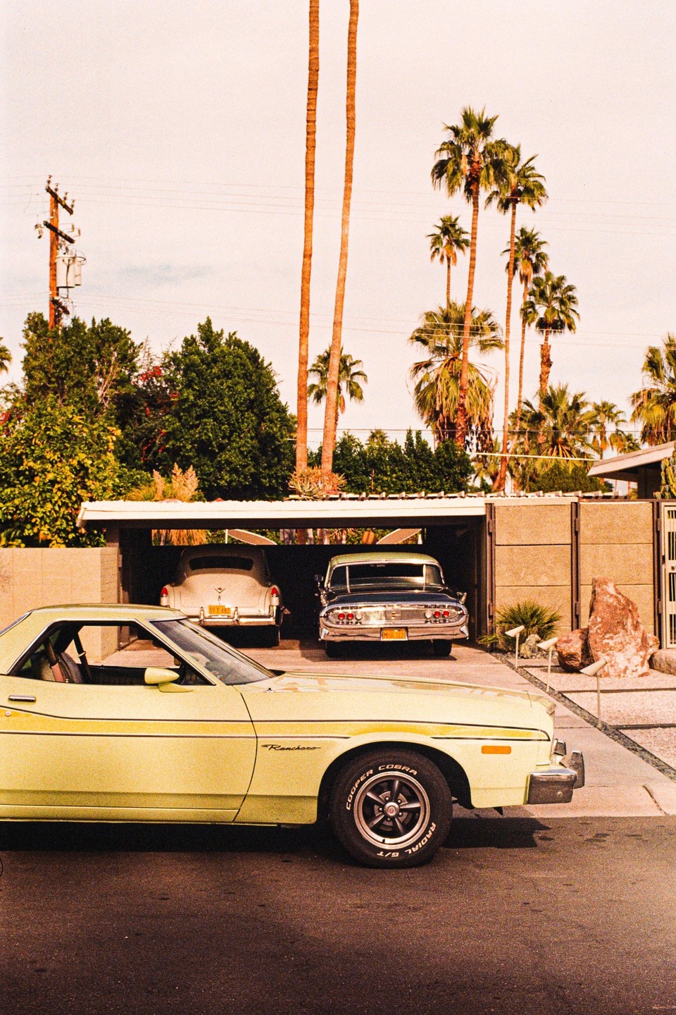 Three vintage cars are parked in front of a house with palm trees under a bright sky.