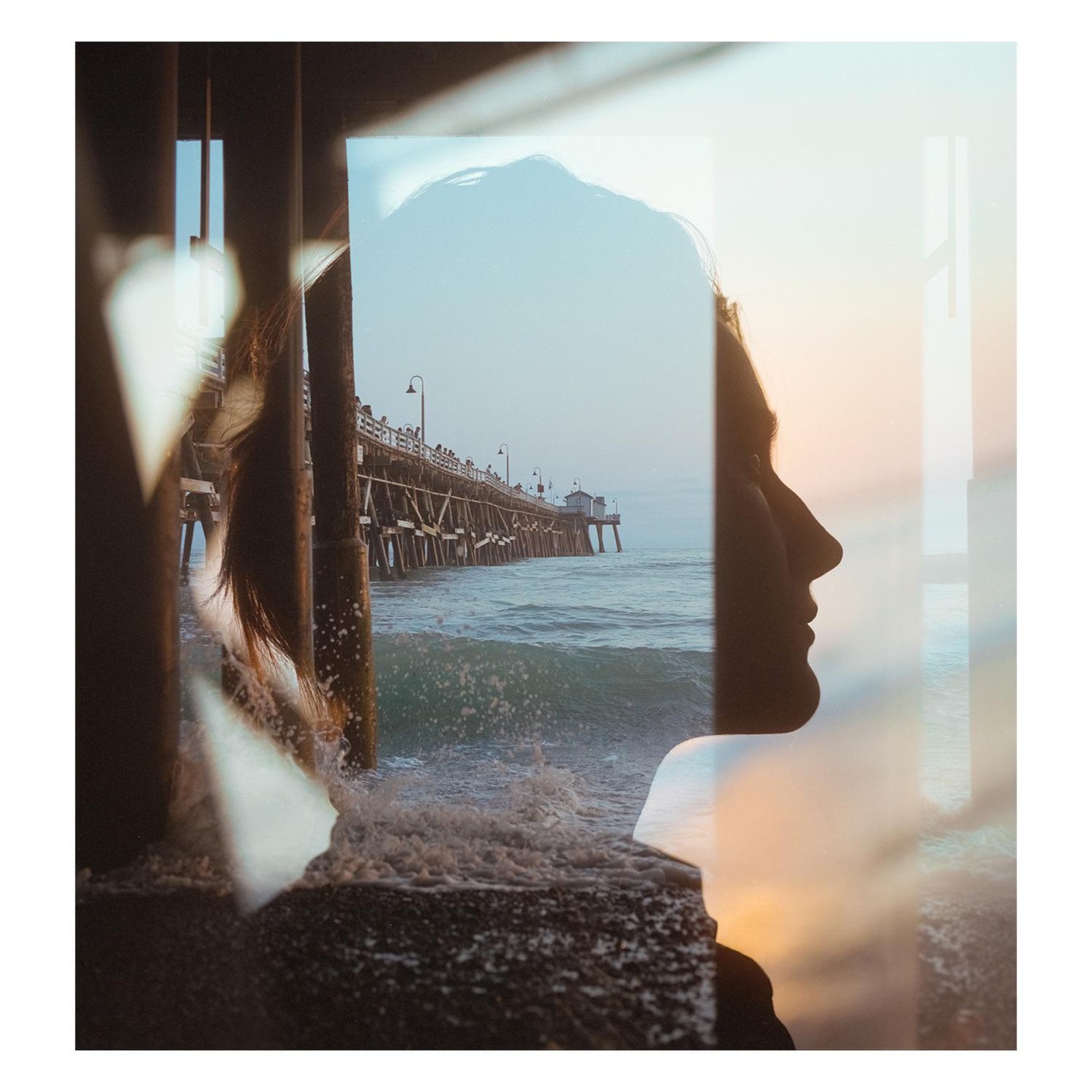 A double exposure shows a woman's silhouette overlaid with a pier extending into the ocean at high tide.
