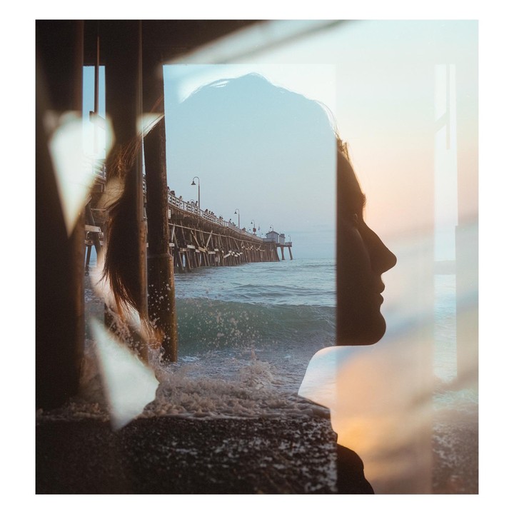 A double exposure shows a woman's silhouette overlaid with a pier extending into the ocean at high tide.
