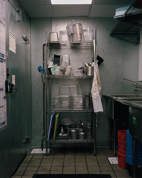 A metal shelving unit filled with various kitchen items stands next to a sink in a commercial kitchen.