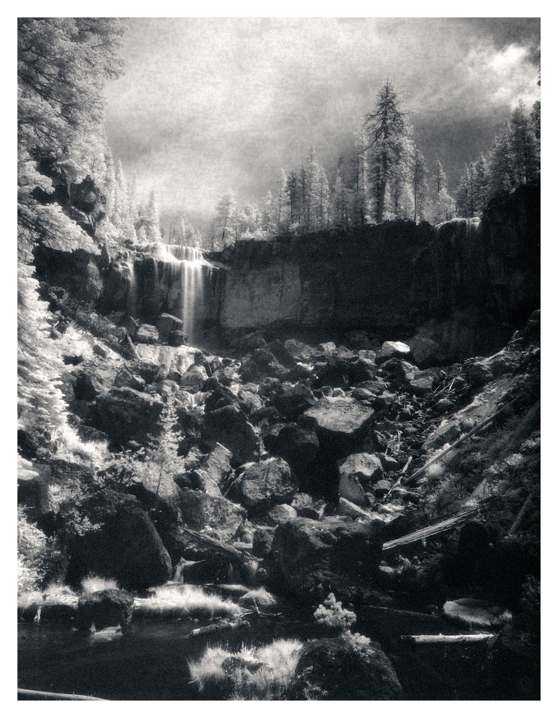 A waterfall cascades over a cliff into a rocky riverbed surrounded by trees.