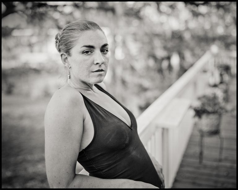 A woman in a swimsuit stands next to a railing, looking directly at the viewer.