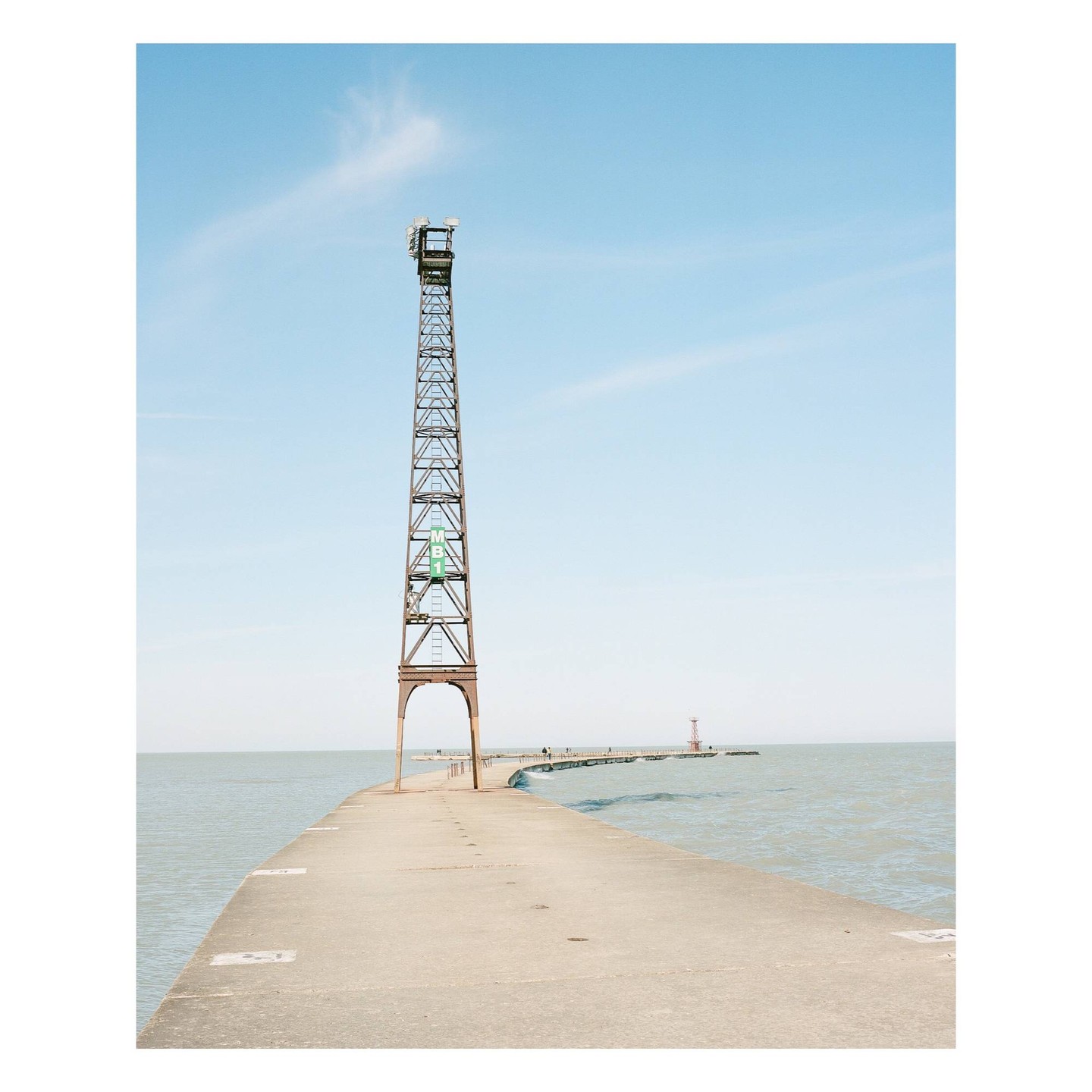 A tall metal tower stands on a concrete pier extending into a body of water under a clear sky.
