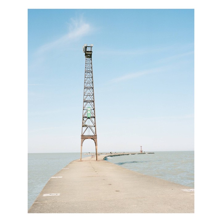 A tall metal tower stands on a concrete pier extending into a body of water under a clear sky.