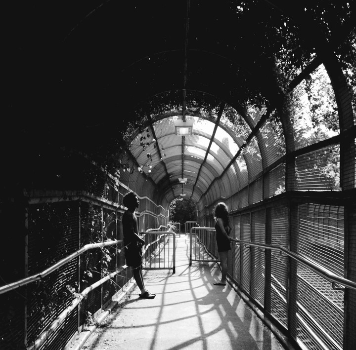 A man and a woman stand in a tunnel with a curved, translucent roof and metal railings.