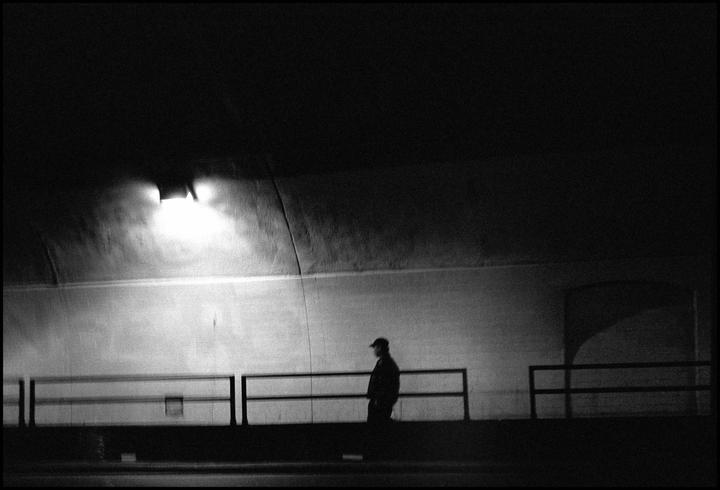 A man walks along a railing in a tunnel lit by a single light.
