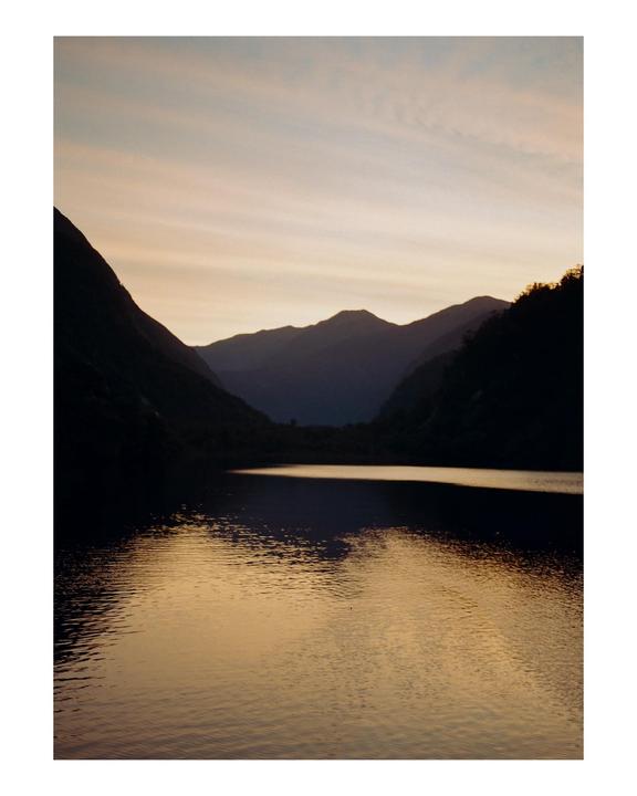 A body of water reflects the sky and mountains at dusk.