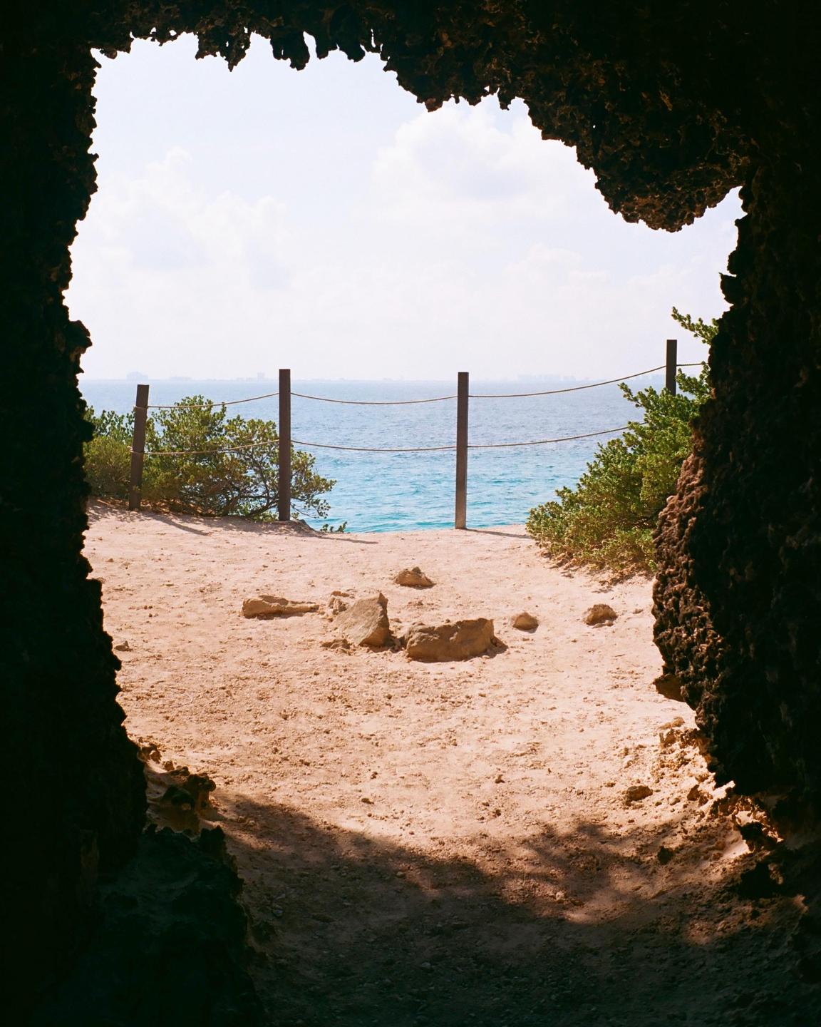 A view of the ocean and a sandy path is framed by a cave opening.