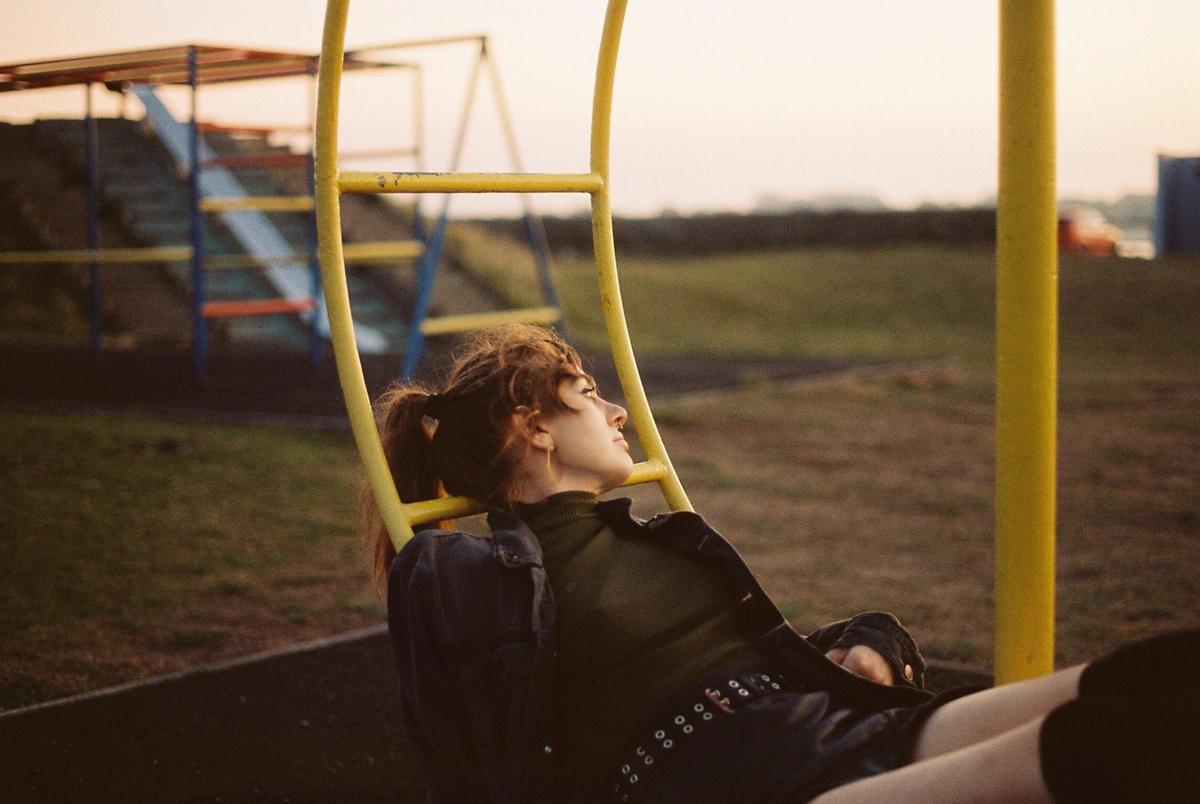 A young woman with a ponytail is sitting on a yellow playground structure, looking up and to the right.