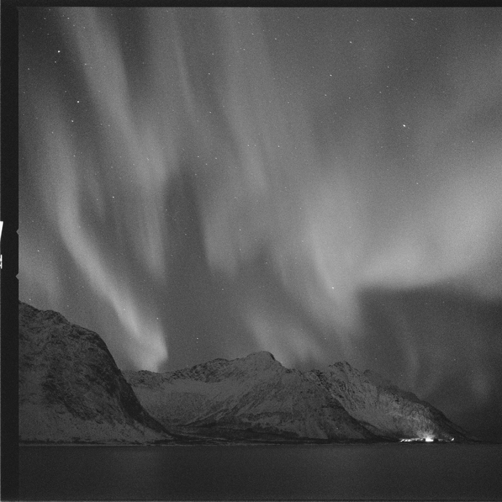 The aurora borealis glows above snow-capped mountains and a body of water at night.