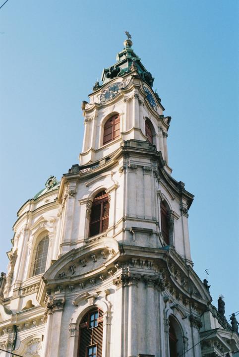 A low-angle shot captures the intricate details of a baroque church tower against a clear blue sky.