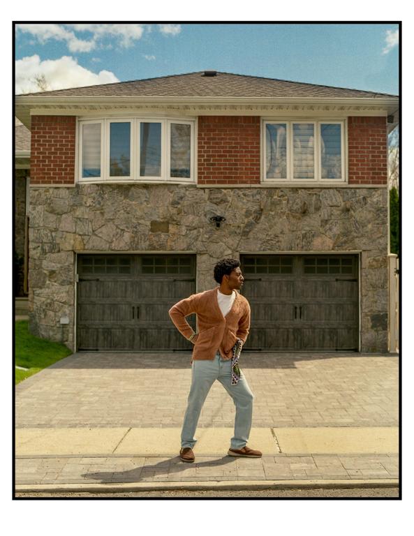 A man stands on a paved driveway in front of a house with a brick and stone facade.