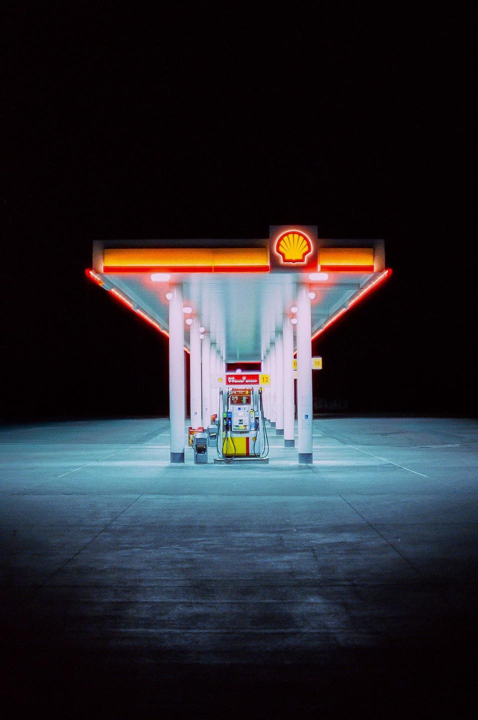 A gas station with a Shell logo is illuminated at night.