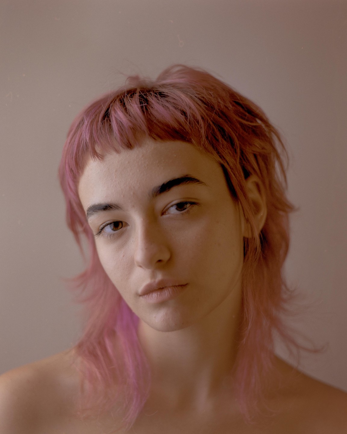 A woman with pink hair and bangs looks directly at the viewer.
