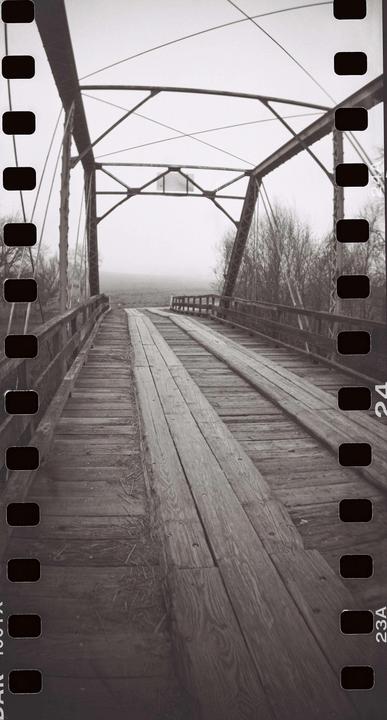 A wooden and metal bridge extends into a hazy distance, flanked by bare trees.