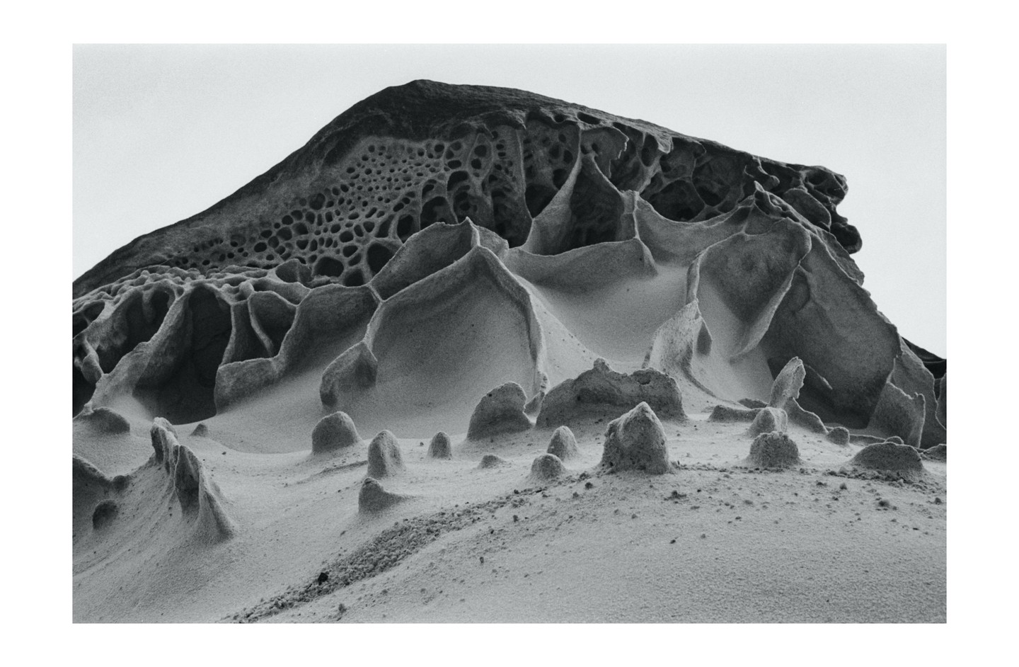A large rock formation with a honeycomb pattern on its upper part and smaller, eroded formations in the foreground is shown.