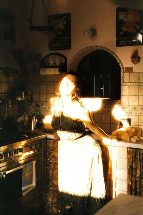 A woman stands in a kitchen with sunlight streaming in, illuminating her face and dress.