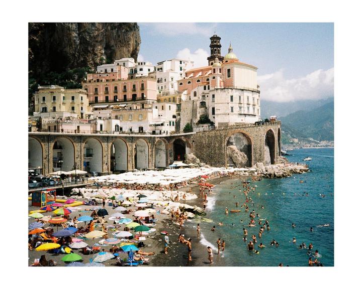 A crowded beach with colorful umbrellas is visible next to a town built into a cliffside.