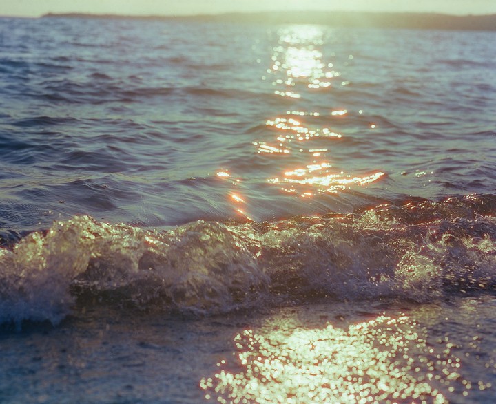 Sunlight reflects off the surface of the ocean as a small wave breaks in the foreground.