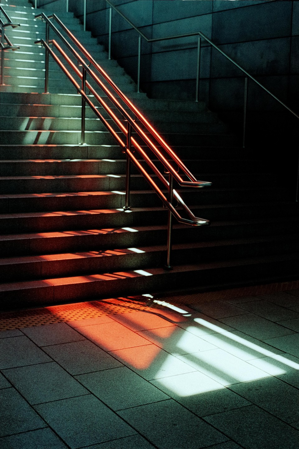 Sunlight casts shadows and red reflections on a concrete staircase with metal railings.