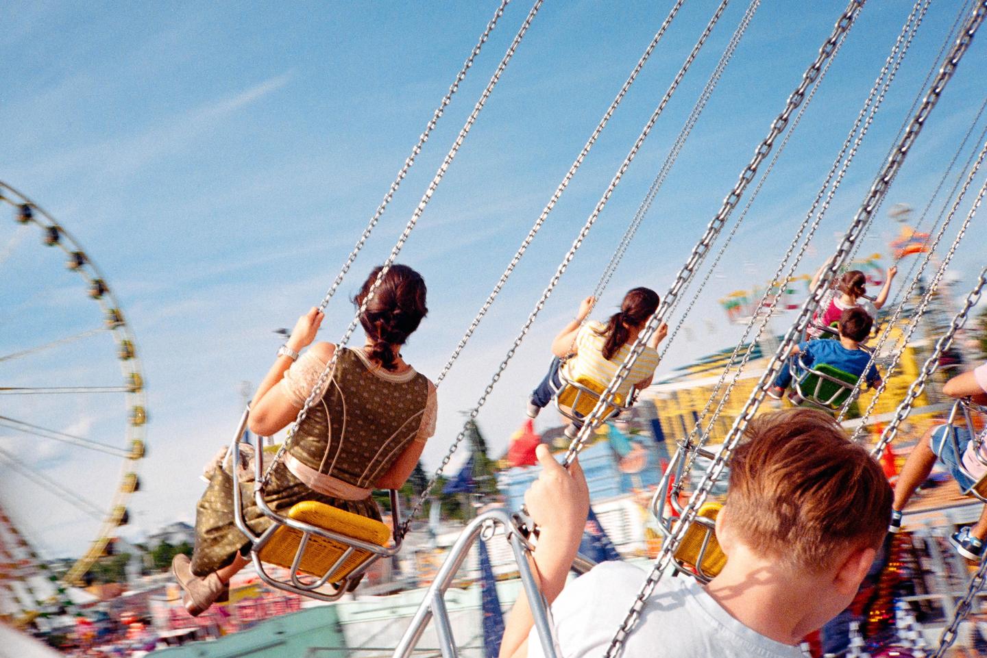 People ride a swing ride at a fairground with a ferris wheel in the background.