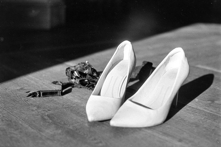 Two high-heeled shoes and a garter belt are on a wooden floor with a strong shadow.