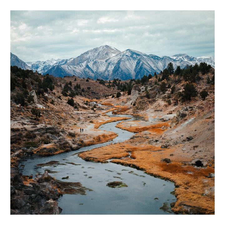A winding river flows through a valley with snow-capped mountains in the background.