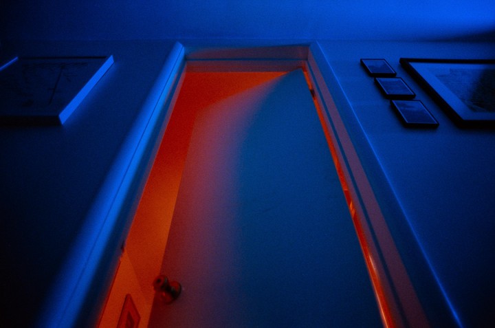 A door is ajar, revealing a bright orange light from the room beyond, contrasting with the blue light in the foreground.