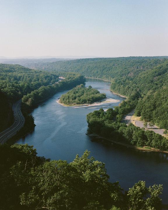 A winding river flows through a valley surrounded by lush green forests and roads.