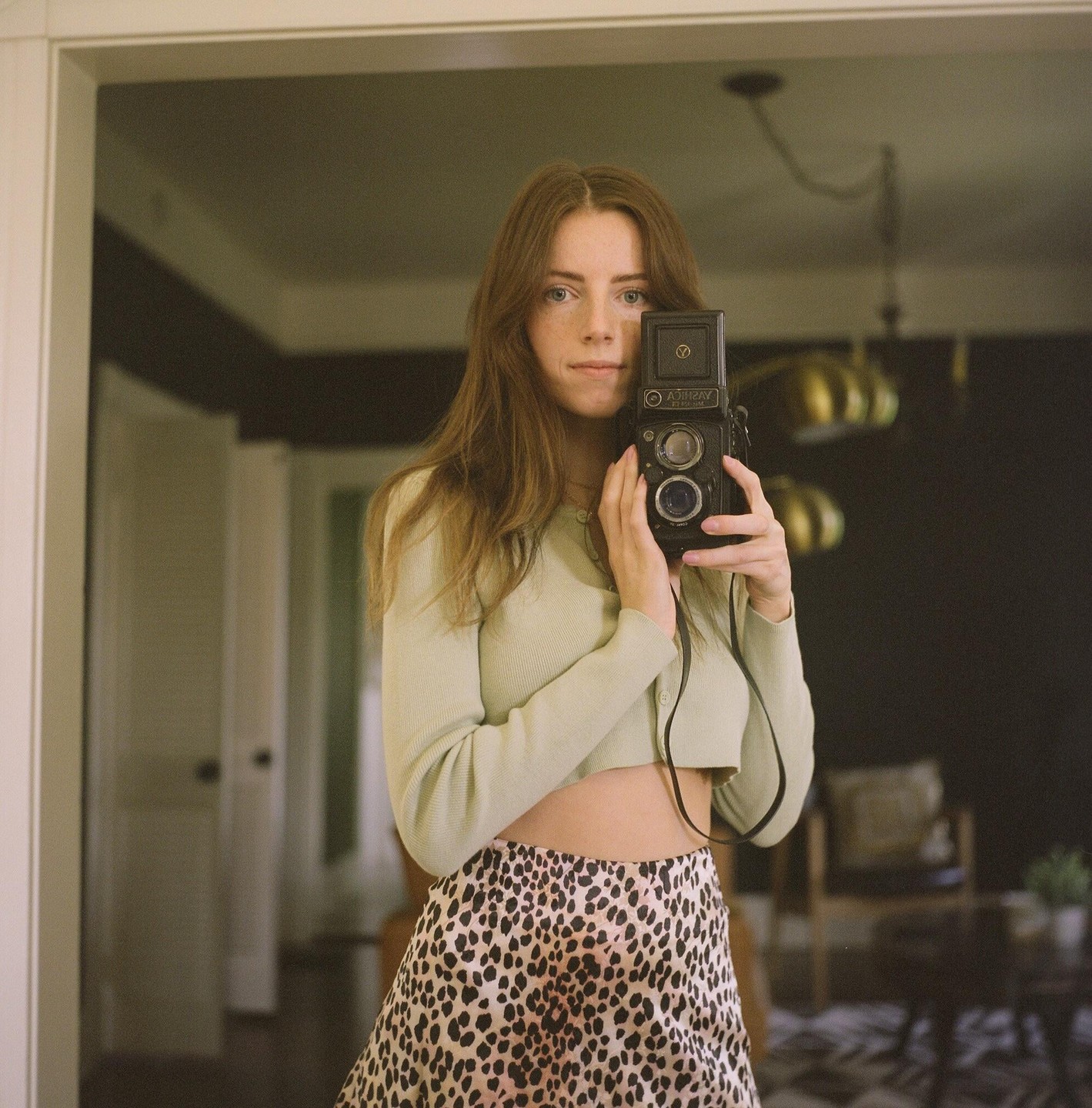 A woman holds a camera to her face while taking a self-portrait in a mirror.