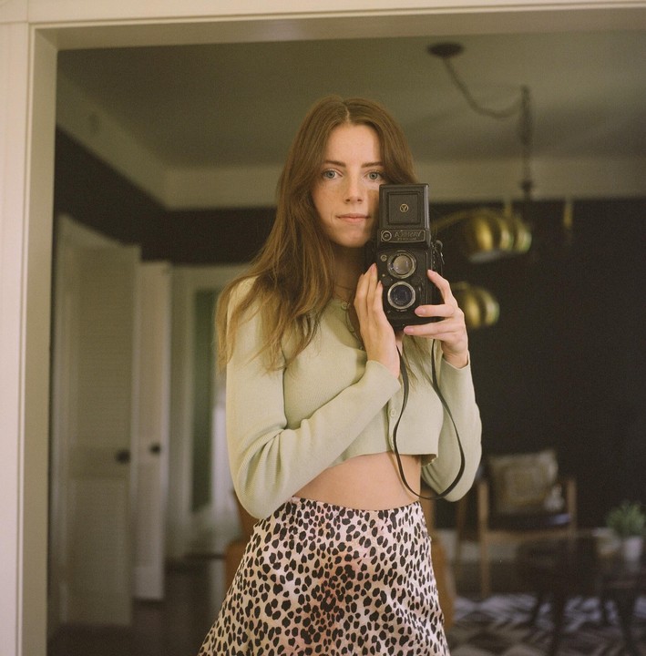 A woman holds a camera to her face while taking a self-portrait in a mirror.