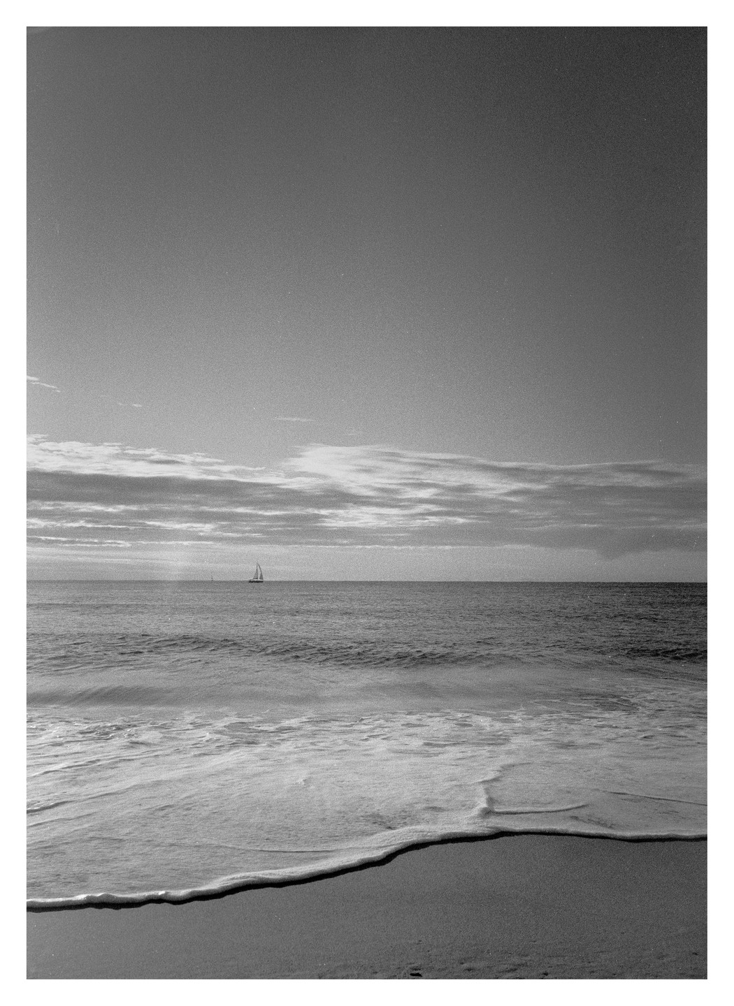 A sailboat is visible on the horizon of a calm sea with a sandy beach in the foreground.