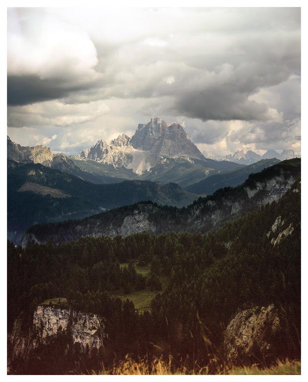 A dramatic mountain landscape is visible under a cloudy sky, with forests in the foreground and a prominent peak in the distance.