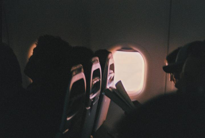 The interior of an airplane cabin is visible with passengers silhouetted against a bright window.